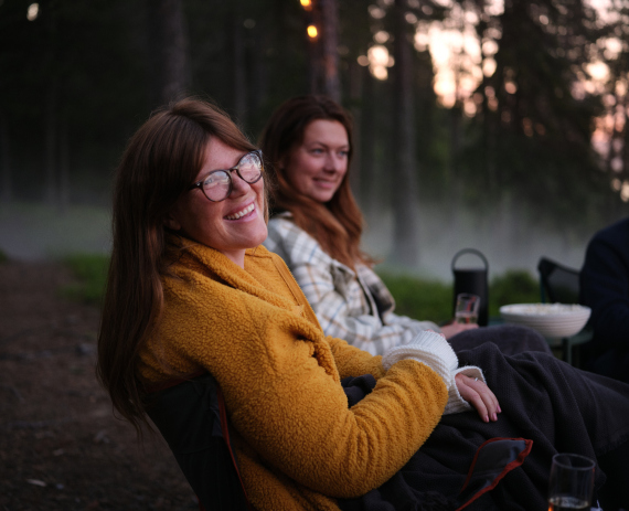 Kaksi henkilöä istumassa ulkona metsäisessä ympäristössä